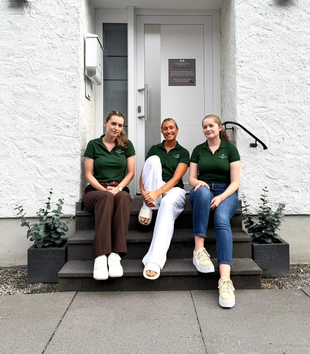 Das Team der Tierphysiotherapie Frankfurt sitzt lächelnd auf der Treppe vor der Praxis